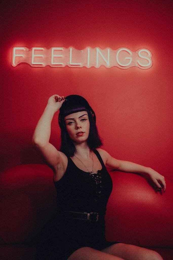 Woman posing in a red room under a neon sign reading 'FEELINGS'.